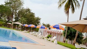 A swimming pool with lounge chairs and umbrellas, surrounded by palm trees and a building with a striped facade.