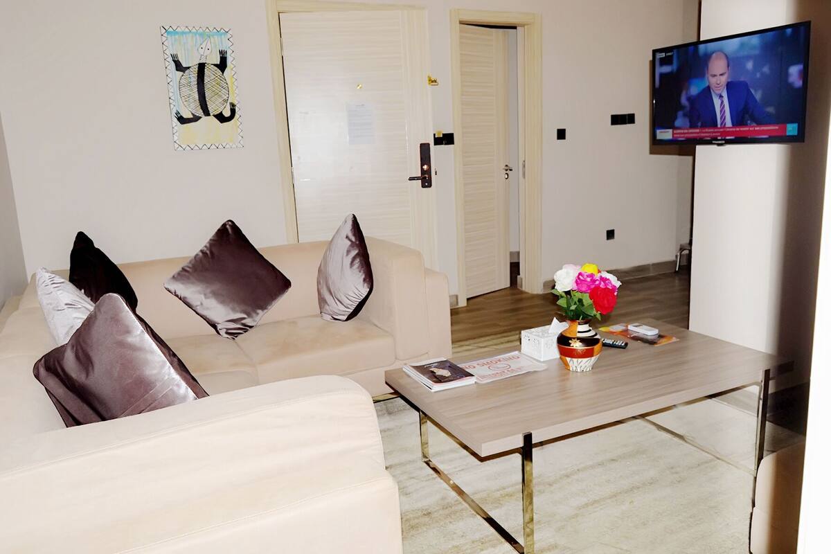 A modern living room with a beige sofa, a coffee table with a vase of flowers, and a television on a stand.