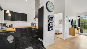 A modern kitchen with black cabinets, a wooden countertop, and a black-tiled floor. There is a large wall clock, a coffee machine, and a kettle on the counter. - Amazing home in Brovst with kitchen (Brovst)