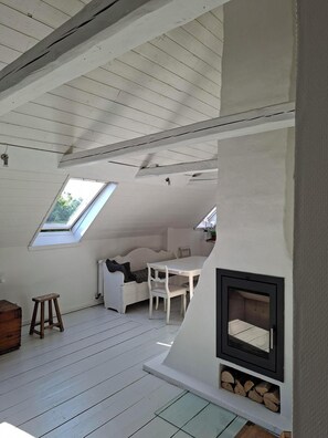 Un espacio tipo loft con techo inclinado, tragaluces, chimenea, sofá blanco y una mesa de comedor.
