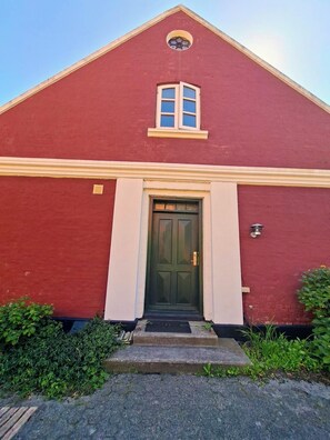 A red building with a green door, a small window, and a light fixture on the wall.