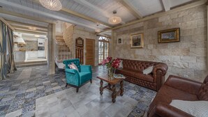Un vaste espace de vie agrémenté d’un mur en pierre, d’un canapé en cuir marron, d’un fauteuil turquoise et d’une table basse en bois.