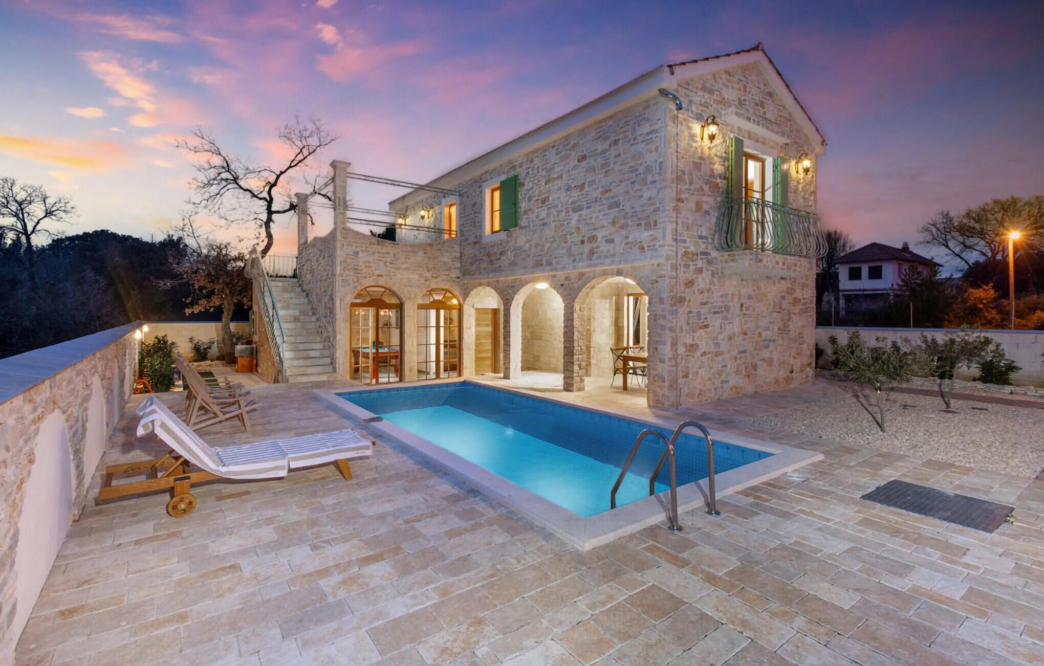 Una villa in pietra con piscina, area salotto esterna e una scala che conduce ai piani superiori.