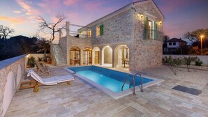 Une villa en pierre dotée d’une piscine, d’un espace extérieur aménagé et d’un escalier menant aux étages supérieurs.