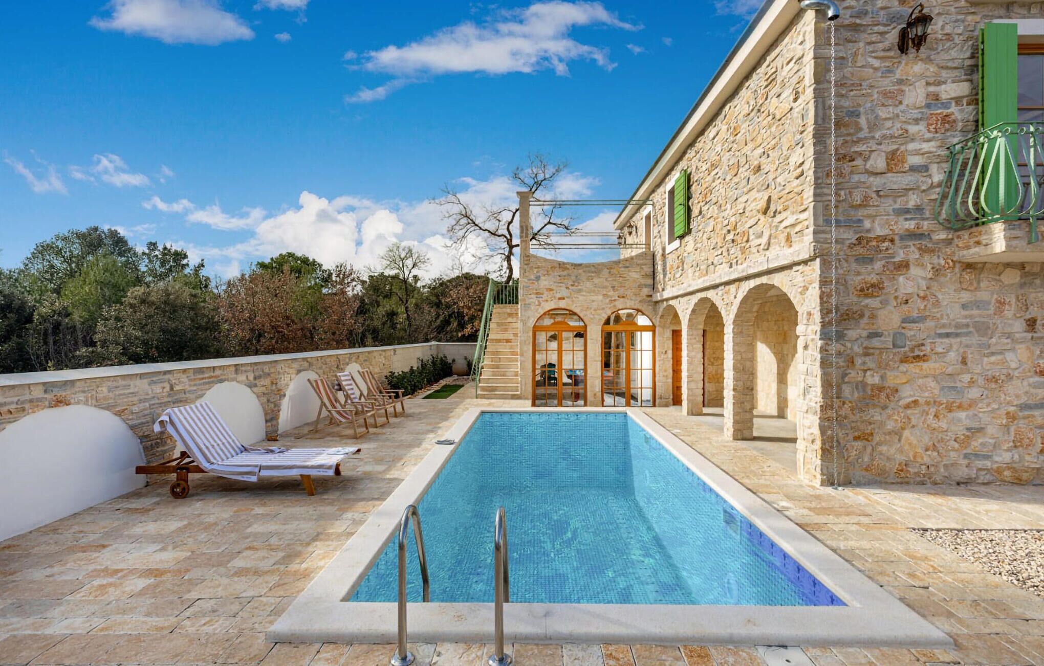 Un edificio de piedra con piscina, zona de estar exterior y una escalera que lleva a un nivel superior.