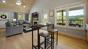 A spacious living area with a high ceiling, a fireplace, and large windows offering a view of the outdoors. - Private Cabin • Hot Tub • Relaxing Smoky Getaway (Sevierville)