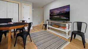 A dining area with a wooden table and chairs, a television on a white stand, and a painting of a landscape on the wall. - Private Cabin • Hot Tub • Relaxing Smoky Getaway (Sevierville)