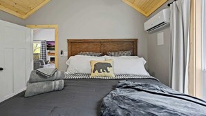 A bedroom with a sloped ceiling, a bed with checkered bedding, a pillow with a bear design, and an air conditioning unit. - Private Cabin • Hot Tub • Relaxing Smoky Getaway (Sevierville)