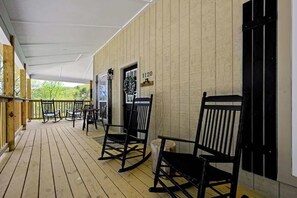 Een overdekt terras met houten vloer, zwarte schommelstoelen en een deur met het nummer 1120.