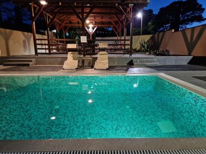 Una piscina con decorazioni in piastrelle, circondata da lettini e un'area relax coperta con tetto.