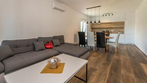 Ein modernes Wohnzimmer mit einem grauen Ecksofa, einem weißen Couchtisch und einem Essbereich mit Holztisch und Stühlen.