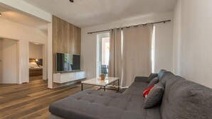 Ein modernes Wohnzimmer mit einem grauen Ecksofa, einem Flachbildfernseher auf einer weißen Kommode und einer Wandpaneele aus Holz.