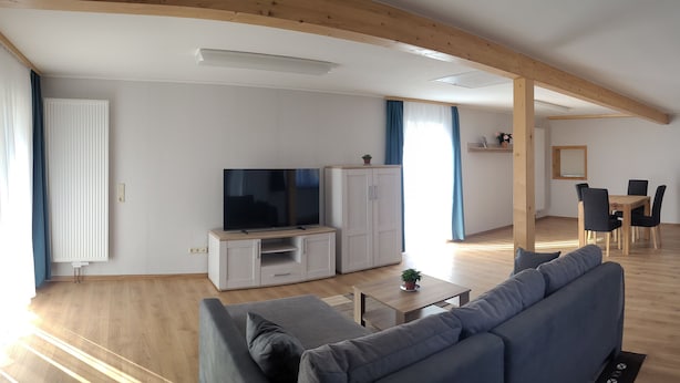 A modern living room with a flat-screen TV, a sofa, a dining table with chairs, and a kitchen area with cabinets. - Vacation home in a quiet location with field view near Lake Leppinsee (Mirow OT Qualzow)