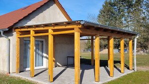 A building with a red roof, a covered porch with wooden beams, and a door with glass panels. - Vacation home in a quiet location with field view near Lake Leppinsee (Mirow OT Qualzow)