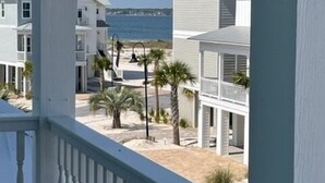 Une vue sur la côte depuis un balcon doté de balustrades blanches, donnant sur une plage bordée de nombreux bâtiments blancs et de palmiers.