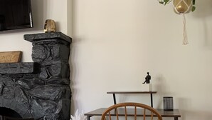 Ein gemütliches Wohnzimmer mit Kamin aus Stein, einem Holzstuhl, einem kleinen Tisch und einer hängenden Pflanze.