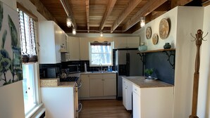 Eine kompakte Küche mit Holzboden, weißen Schränken, einer zentralen Kochinsel und einer hängenden Leuchte.
