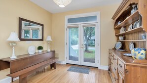Un couloir avec un banc en bois, une porte blanche dotée de panneaux de verre et un meuble en bois orné d’assiettes décoratives.