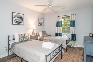 A bedroom with two beds, a ceiling fan, a nightstand with a lamp, and a window with curtains.