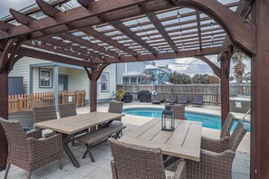 Une terrasse extérieure agrémentée d’une pergola en bois, d’une piscine et de mobilier en osier.