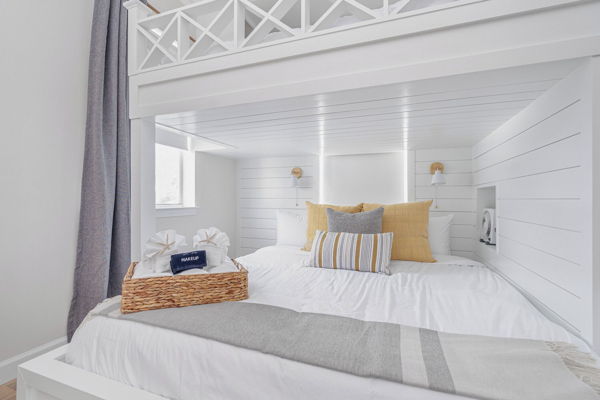 A white, modern bedroom with a bed, pillows, a bedside table, and a lamp.
