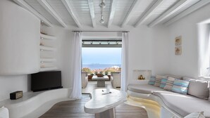 A modern living room with a stone table, white sofas, a flat-screen TV, and a view of the sea. - El Sueno Villa Mykonos (Mykonos)