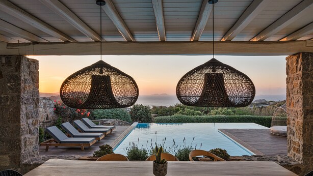 A poolside area with lounge chairs, a table, and hanging wicker lamps. - El Sueno Villa Mykonos (Mykonos)