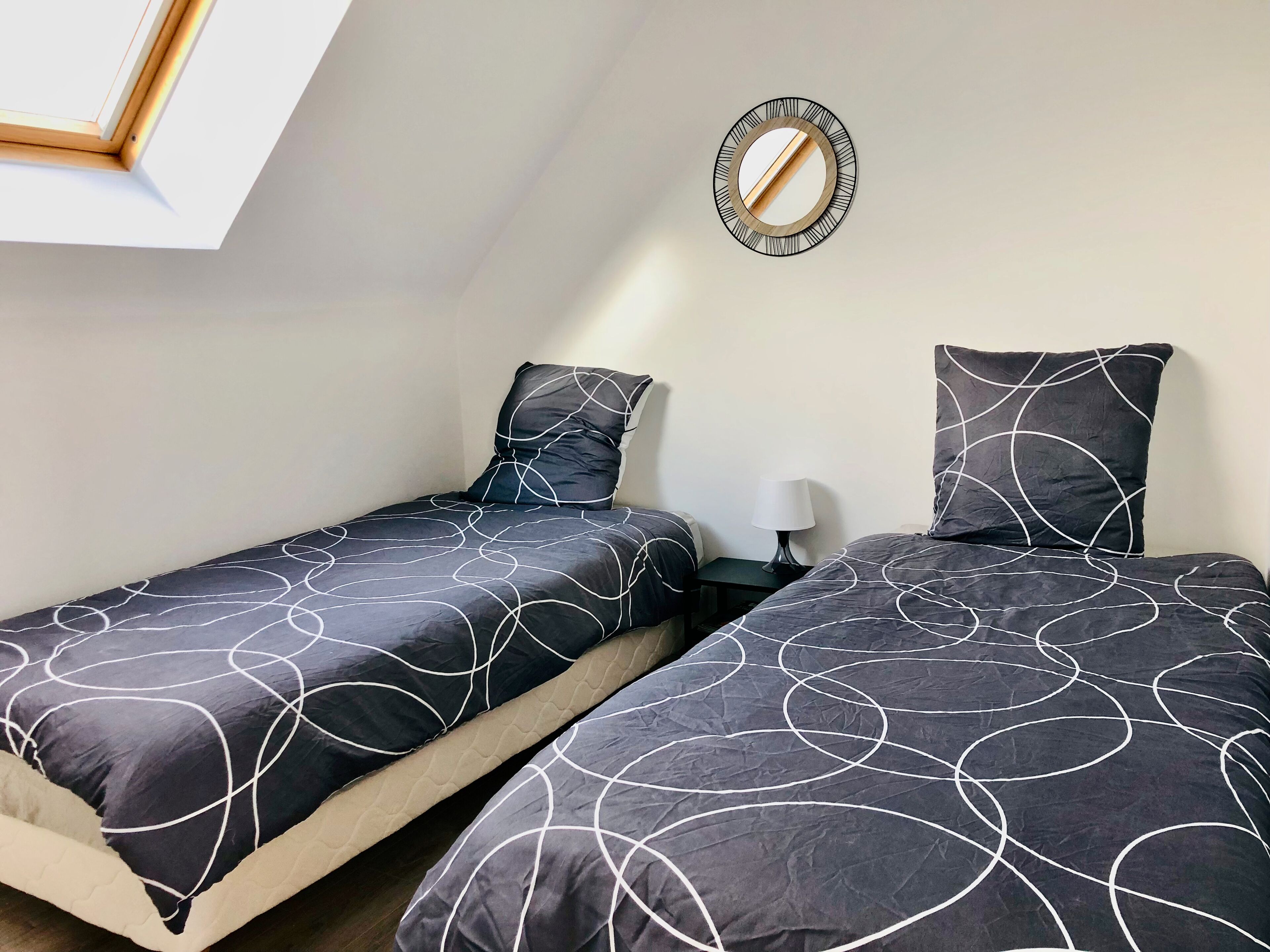 Une chambre avec deux lits, une table de chevet avec une lampe et un miroir fixé au mur.
