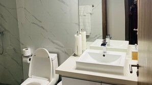 A modern bathroom with a toilet, two sinks, a mirror, and a shower.