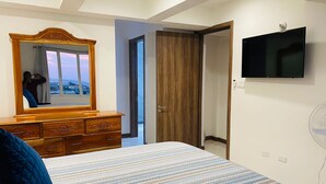 A bedroom with a bed, a dresser, a TV, and a door leading to another room.