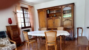A dining area with a round table, wooden chairs, a cabinet with shelves, and a window with curtains. - Charming house at the gateway to the Ardèche (Pont-Saint-Esprit)