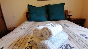 A bed with a white bedspread featuring bamboo designs and Chinese characters, two green pillows, and two rolled towels on the bed. - Charming house at the gateway to the Ardèche (Pont-Saint-Esprit)