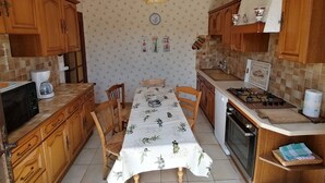A compact kitchen with wooden cabinets, a dining table with a floral tablecloth, a microwave, a stove, and a sink. - Charming house at the gateway to the Ardèche (Pont-Saint-Esprit)