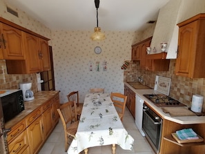 Una cocina compacta con armarios de madera, una mesa de comedor con mantel floral, un microondas, una estufa y un fregadero.