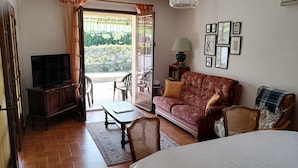 A room with a bed, a sofa, a television, a table, and a chair. There is a door leading to an outdoor area with plants and a table. - Charming house at the gateway to the Ardèche (Pont-Saint-Esprit)