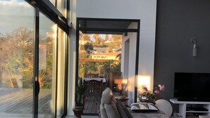 A modern living room with a large glass wall, a sofa, a TV, and a view of the outdoors. - Modern villa full of sun for a great vacation (Biot)