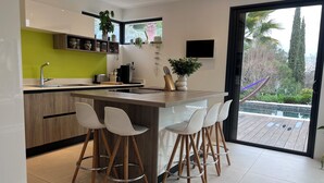 A modern kitchen with a central island, bar stools, a built-in sink, and a large window overlooking a pool. - Modern villa full of sun for a great vacation (Biot)
