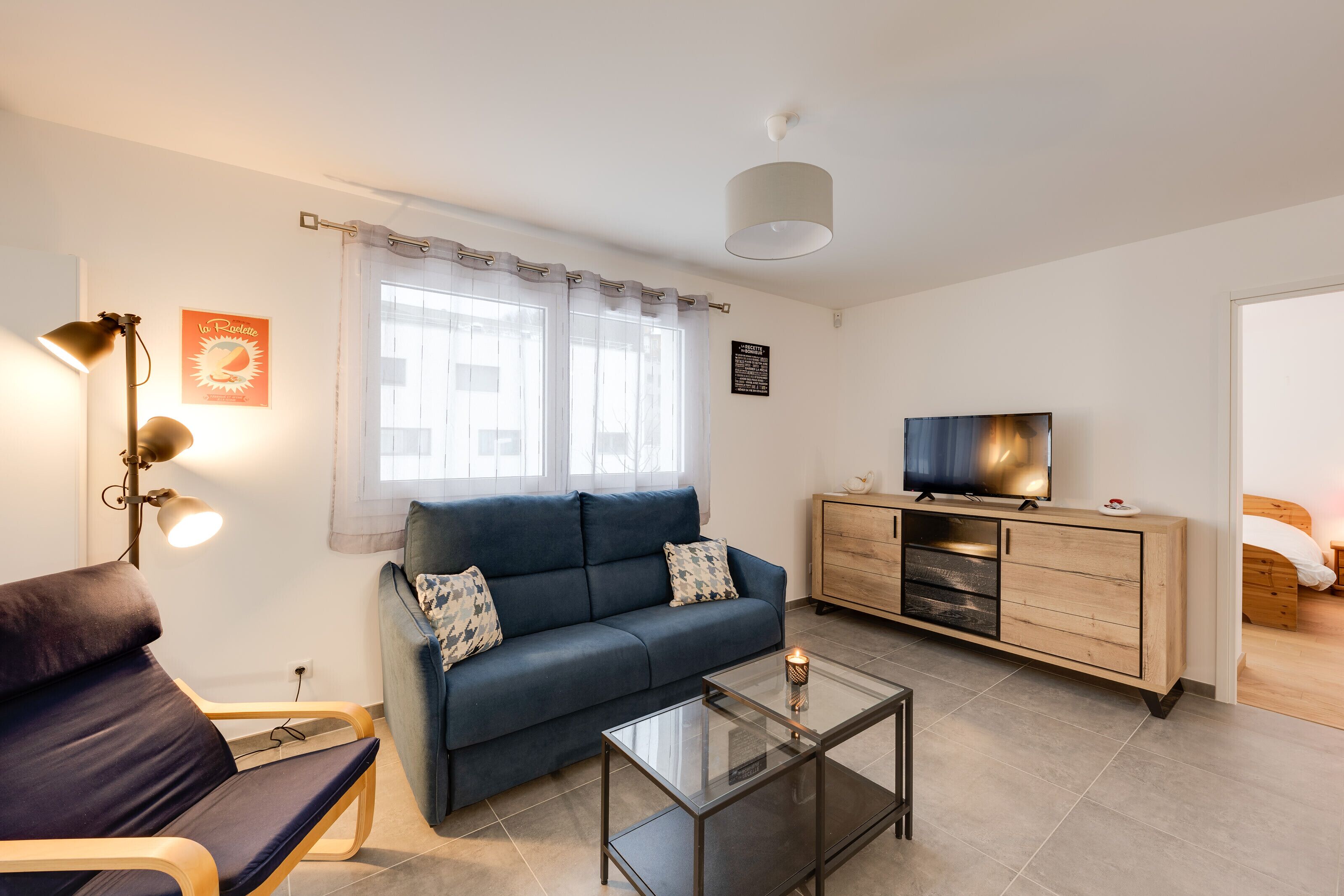 A modern living room with a sofa, a glass coffee table, a TV on a wooden cabinet, and a lamp.