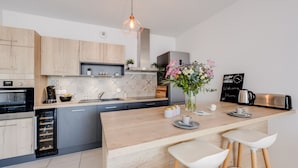 Une cuisine moderne avec un îlot central en bois, des tabourets de bar, un coin café et une horloge au mur.