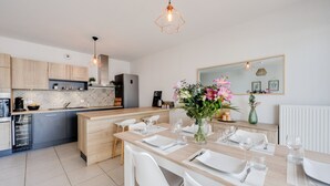 Une cuisine moderne avec un coin repas, comprenant un îlot central, des meubles blancs et un grand miroir au-dessus de l’îlot.