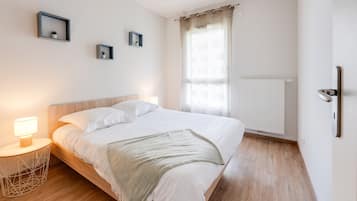 Een keurig opgemaakt slaapkamer met een bed, nachtlampjes, een raam met gordijnen, en een radiator aan de muur.