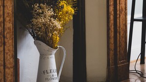 A white vase with flowers placed on a wooden floor near a fireplace with a decorative arch.