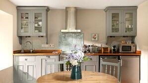 A kitchen with grey cabinets, a stainless steel range hood, a microwave, and a wooden dining table with a vase of flowers. - 5* Luxurious 1 bed self-catering cottage, 20mins from North&South Cornish coasts (Truro)