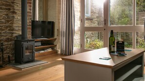 A cozy room with a stone wall, a black wood stove, a television, and a wooden table with a bottle and a sign. - 5* Luxurious 1 bed self-catering cottage, 20mins from North&South Cornish coasts (Truro)