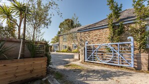 A stone building with a gated entrance, a gravel driveway, and a wooden planter with plants. - 5* Luxurious 1 bed self-catering cottage, 20mins from North&South Cornish coasts (Truro)