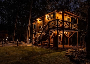 A wooden cabin with a deck and stairs, surrounded by trees.