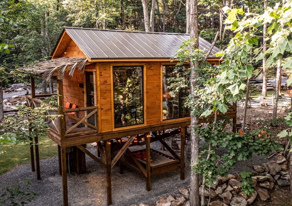 Une cabane en bois avec un toit en métal, entourée d’arbres et bordée d’un chemin de gravier.