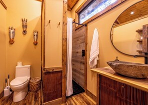 Une salle de bain avec un plancher en bois, des toilettes, un lavabo avec un receveur en pierre et un miroir.