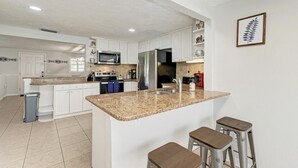 A modern kitchen with white cabinets, granite countertops, stainless steel appliances, and a bar stool area. - Waterfront Home with Private Dock and Kayaks 4 Bedroom 2 Bath (Bradenton)