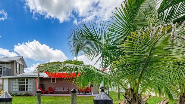 A wooden deck leading to a house with a red roof, surrounded by lush greenery and palm trees. - Waterfront Home with Private Dock and Kayaks 4 Bedroom 2 Bath (Bradenton)